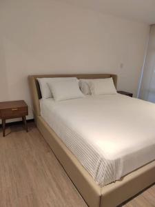 ein Bett mit weißer Bettwäsche und Kissen sowie einem Tisch in der Unterkunft Hermoso apartamento nuevo en zona 10! in Guatemala