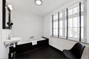 ein Badezimmer mit einem Waschbecken, einer Badewanne und einem Stuhl in der Unterkunft College Hotel Alkmaar in Alkmaar