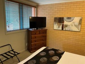 Albury Georgian Motel & Suites في البوري: غرفة نوم مع تلفزيون وسرير وخزانة