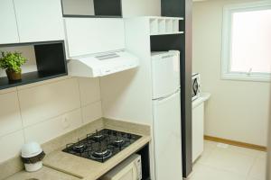 Il comprend une cuisine blanche équipée d'une cuisinière et d'un réfrigérateur. dans l'établissement Incrível Apto De 2 Quartos Em Gramado - Ed Paradiso, à Gramado