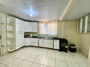a kitchen with white cabinets and a white tile floor at Casa Grande com 2 quartos e 1 suíte in Foz do Iguaçu