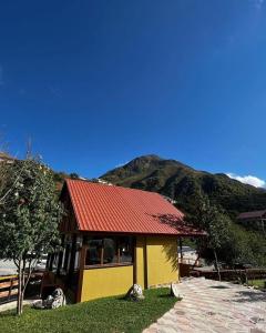 a yellow building with a red roof in front of a mountain at Juta Guest House in Jut'a