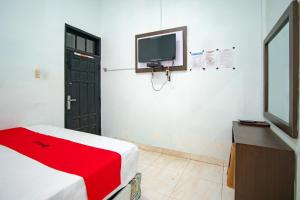 Habitación con TV y cama con manta roja. en RedDoorz Syariah near Danau Lut Tawar Takengon, en Takengon