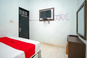 a room with a tv and a bed with a red blanket at RedDoorz Syariah near Danau Lut Tawar Takengon in Takengon
