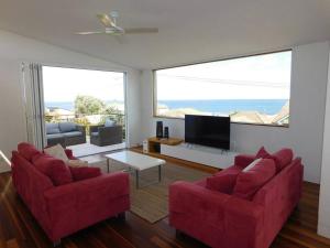 a living room with two red chairs and a flat screen tv at Clovelly Beach House with Pool in Sydney