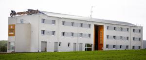 un grand bâtiment blanc avec un champ herbeux devant lui dans l'établissement Sweet and Smart Sarreguemines - Hambach, à Hambach