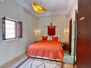 1 dormitorio con cama con sábanas de color naranja y ventana en Riad Jolie en Marrakech