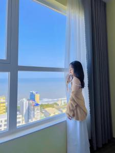 une femme qui parle sur un téléphone portable devant une fenêtre dans l'établissement Goldsea Vũng Tàu - Khang Apartment, à Vung Tau