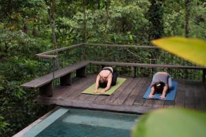 zwei Leute machen Yoga auf einer Brücke neben einem Pool in der Unterkunft Hideaway Village Bali Ubud by Kanaan Hospitality in Ubud