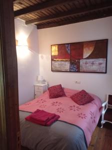 um quarto com uma cama com lençóis cor-de-rosa e almofadas vermelhas em Casa rural Adelaida em Villanueva del Conde