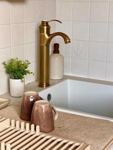 - un lavabo avec un robinet en or, 2 tasses et une baignoire dans l'établissement Chez Romy - studio équipé avec wifi - proche plage Deauville, à Tourgéville