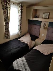 two beds in a small room with a window at 6 BERTH DELUXE CARAVAN PALM GROVE 42 in Chapel Saint Leonards