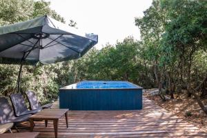 un bain à remous et un parasol sur une terrasse en bois dans l'établissement The Scandinavian Village-Teva BaHar, à H̱aluẕ