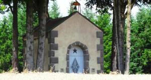 una pequeña capilla con una puerta azul y árboles en La p'tite Bohème, en Gouttières