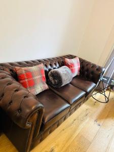 a brown leather couch with pillows on a wooden floor at 1 bedroom apartment in Shepherds Bush, London in London