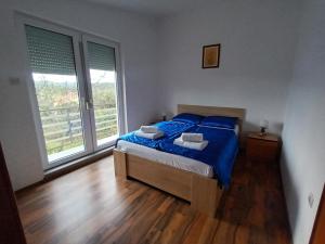 een slaapkamer met een bed met blauwe lakens en 2 ramen bij Apartman Štrkalj in Tisno