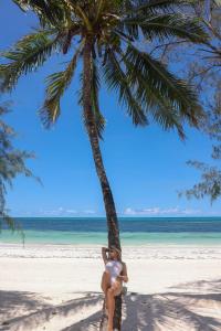 a woman sitting on a palm tree on the beach at F-Zeen Boutique Hotel Zanzibar in Uroa