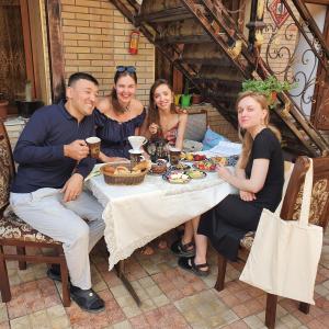 un grupo de personas sentadas alrededor de una mesa con comida en Sherxan House, en Samarkand