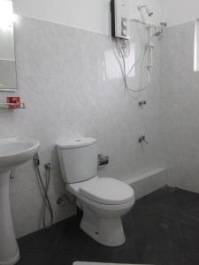 a white bathroom with a toilet and a sink at Hotel Oviya in Vavuniya
