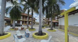 a courtyard with palm trees and white chairs at Chalé Aconchego in Barreirinhas