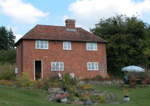 una casa de ladrillo rojo con mesa y sombrilla en Orchard Cottage en Sutton Valence