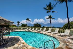 a swimming pool with chairs and the ocean in the background at Keauhou Akahi 302 in Kailua-Kona