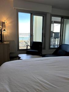 a bedroom with a bed and two chairs and windows at Appartement vue mer in Soulac-sur-Mer