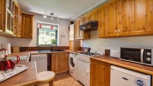 cocina con armarios de madera, lavadora y secadora en Wayside Cottage en Tansley