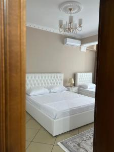 a white bedroom with a white bed and a chandelier at SaEl Apartments in Shkodër