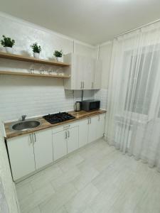 cocina con armarios blancos, fregadero y ventana en Дизайнерская квартира в центре города, en Petropavlovsk