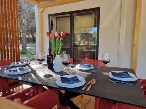 Premium mobile home SUN & JOY - Oaza Mira Camping في دراغ: طاولة سوداء مع كراسي حمراء وكؤوس للنبيذ