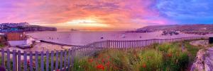 vistas a una playa con una valla y flores en Luxury Sunrise to Sunset Beachfront Apartment, en Perranporth
