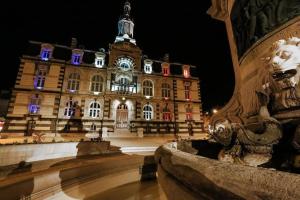 un bâtiment avec une fontaine devant lui la nuit dans l'établissement Les Ateliers d'Art, à Roanne