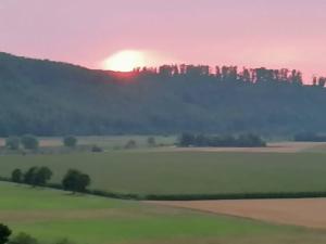 a sunset over a field with the sun rising behind a hill at FeWo mit Weser-Fernblick in Hehlen