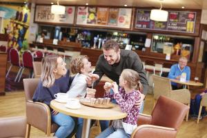 un hombre y dos niños sentados en una mesa comiendo pastel en Sunny Hunny Manor Park Caravan, en Hunstanton