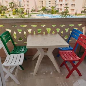 einen weißen Tisch und vier bunte Stühle auf dem Balkon in der Unterkunft شاليه راقي بمارسيليا بيتش 1 الساحل in Dawwār Muḩammad Abū Shunaynah