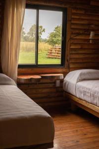 1 dormitorio con 2 camas y una ventana en una cabaña de madera en Cabañas El Sosiego en Azul