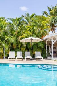 een zwembad met stoelen en een parasol en palmbomen bij TUK Tropical Boutique Resort Jan Thiel in Willemstad