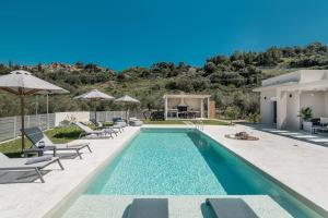 a swimming pool with chairs and umbrellas next to a house at Melissia Luxury Villa in Zakynthos Town