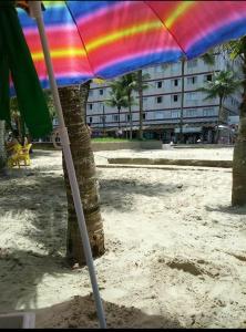 a rainbow colored umbrella on a sandy beach at Lindo apartamento em frente a praia in Praia Grande