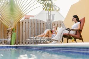 two women sitting on chairs by a pool with a laptop at Bario Hotel in Willemstad
