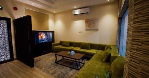 a living room with a green couch and a tv at شاليهات وفلل ريلاكس بلاس in Sirr Āl Ghalīz̧