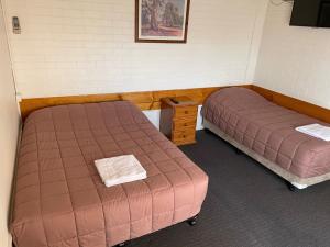 a room with two beds and a night stand and avertisement at Homestead Motel in Dubbo