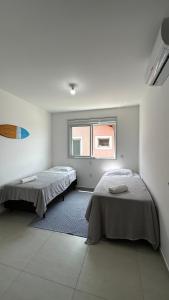 Duas camas num quarto branco com uma janela em Casa em Floripa - 200m da praia em Florianópolis