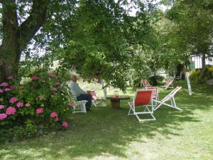 Ein Mann, der in einem Garten mit Stühlen und einem Tisch sitzt. in der Unterkunft La Longère Aux Sapins in Fontaine-le-Bourg