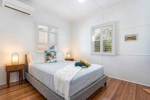 a white bedroom with a bed and two windows at Stylish 1950s Moffat Beach House in Caloundra