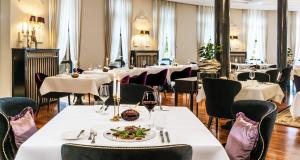 um restaurante com mesas e cadeiras brancas e um prato de comida em Victor's Residenz-Hotel Schloss Berg em Nennig