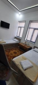 Cette chambre comprend 2 lits, une table et 2 fenêtres. dans l'établissement KAMIR Guest House, à Boukhara