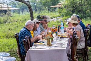 eine Gruppe von Menschen, die an einem langen Tisch sitzen in der Unterkunft Serengeti Wild Camp in Serengeti-Savanne