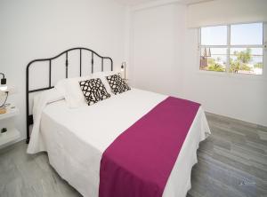 a white bedroom with a large bed with a purple blanket at Balcón a Doñana in Sanlúcar de Barrameda